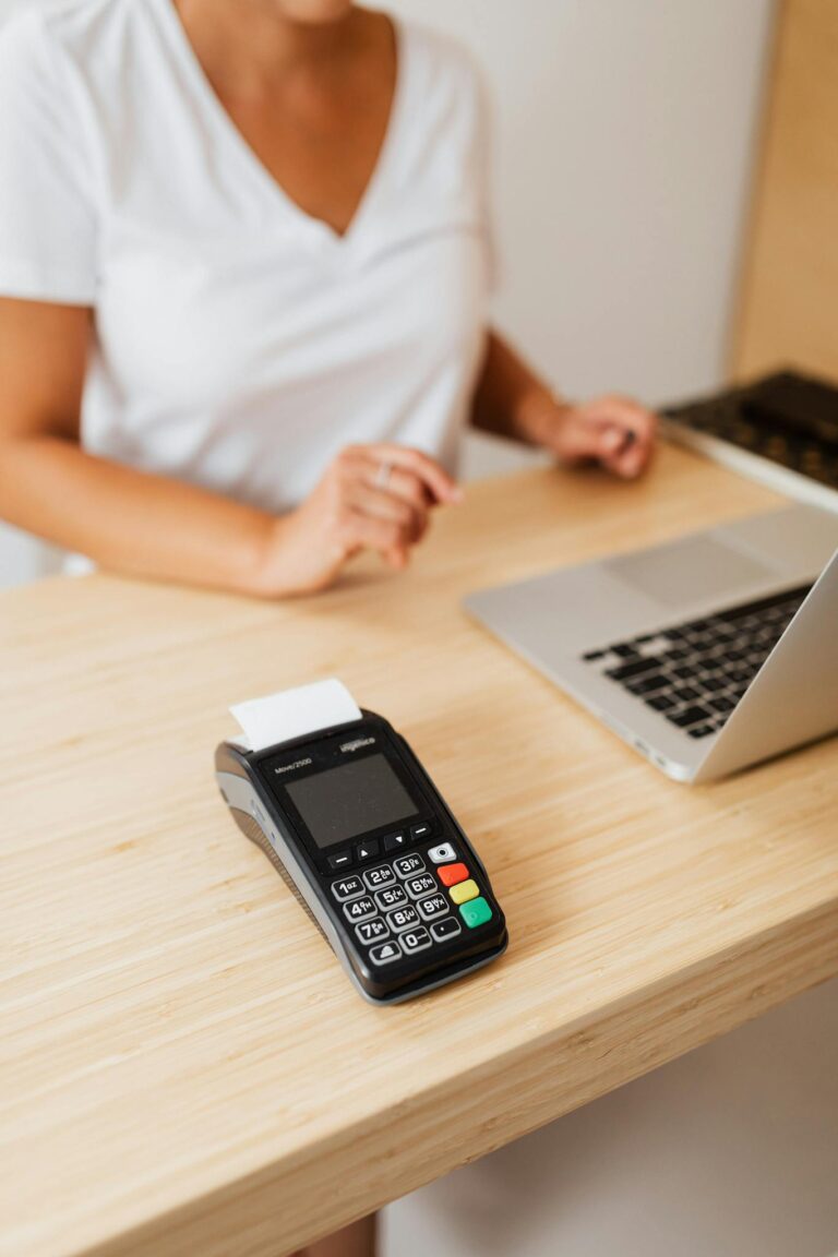 A cashier processes a cashless transaction using a payment terminal and laptop at a retail counter.